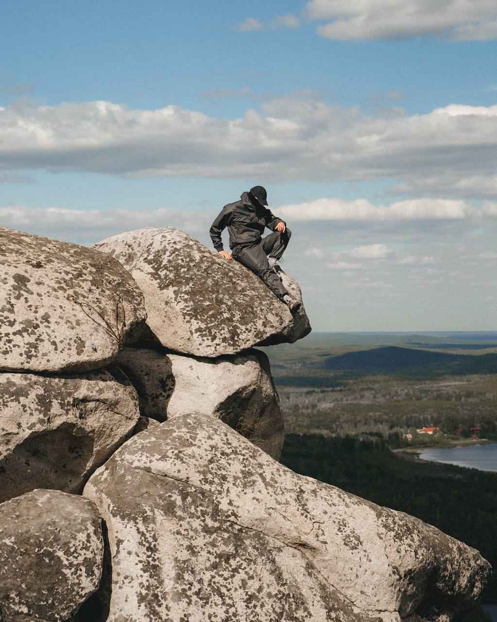 Изобрежние человека, сидящего на скале в фирменной одежде НЕАЛИТ